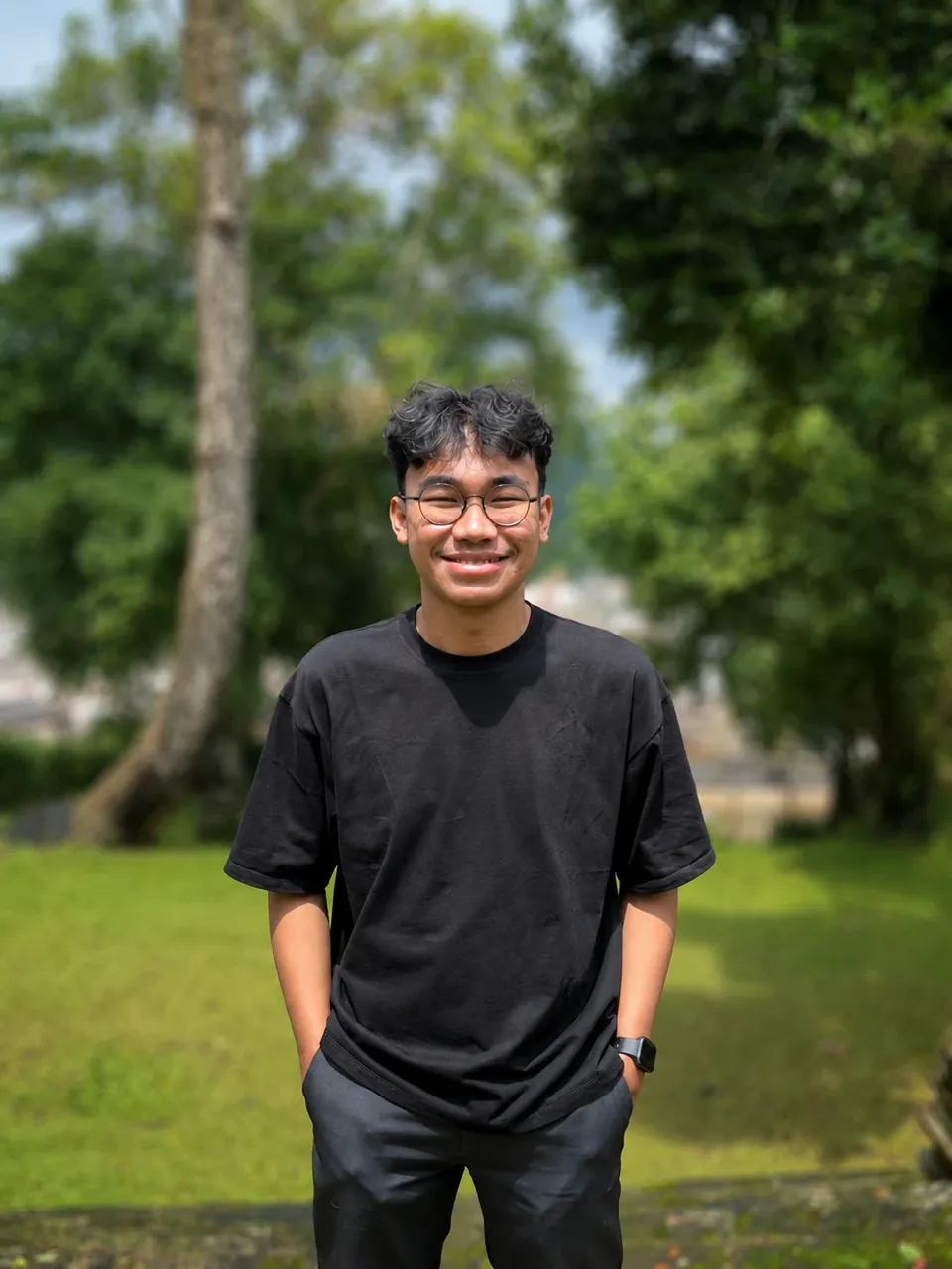 Reihan Renaldi smiling, in a black T-shirt, standing on a lawn in front of trees